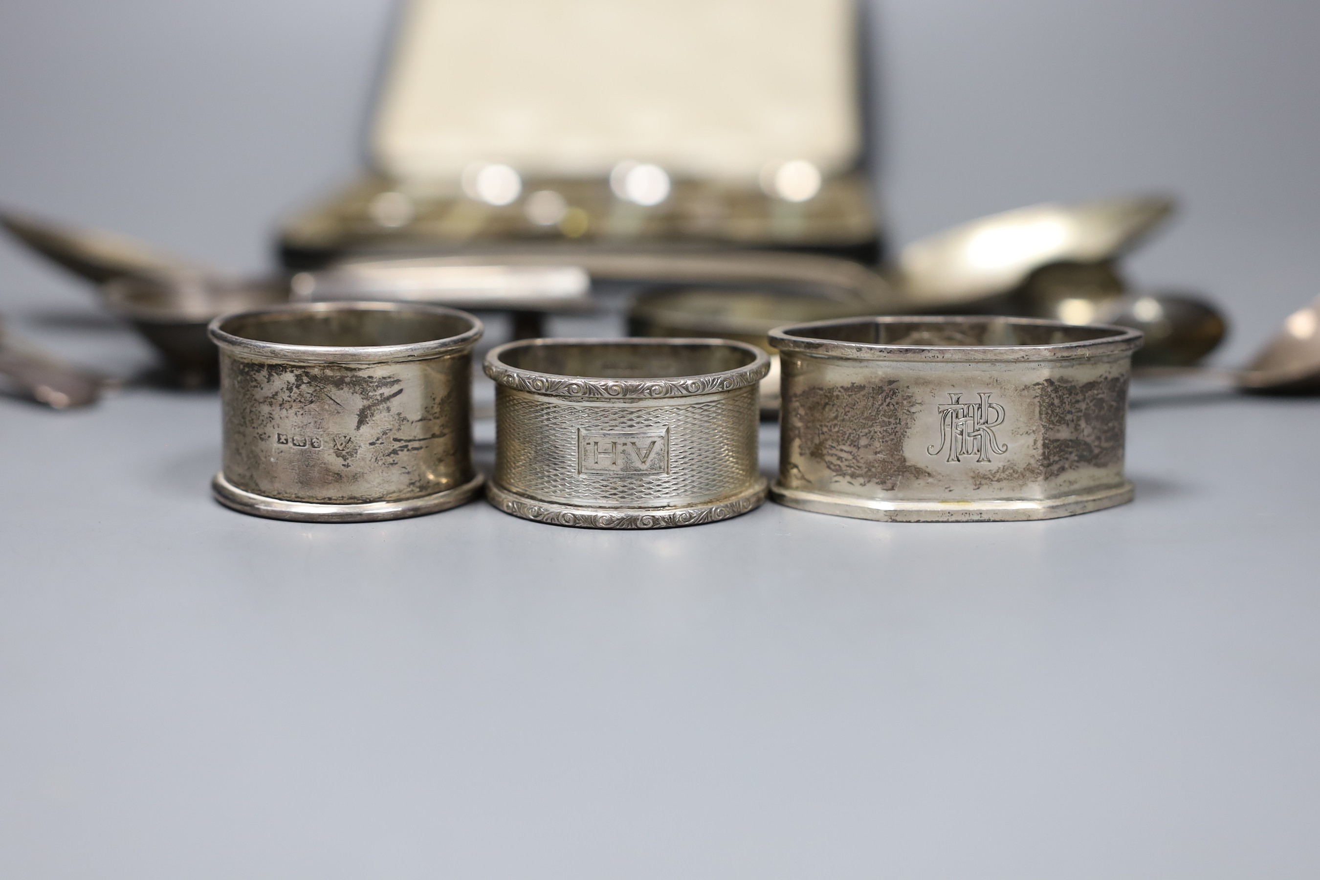 A pair of George III bright cut silver table spoons, three later assorted napkin rings, a cigar stand, a pair of tongs, five assorted spoons, 10oz., and a cased set of silver and enamel coffee spoons